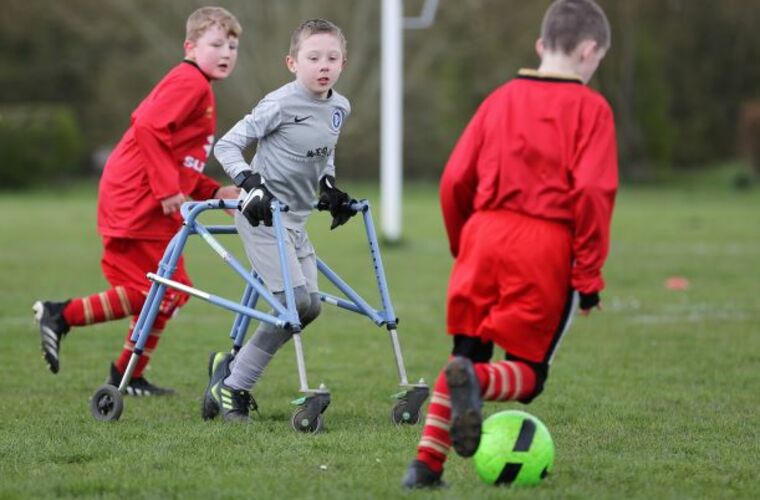 Three boys playing in a football match, one player is using a frame walker.