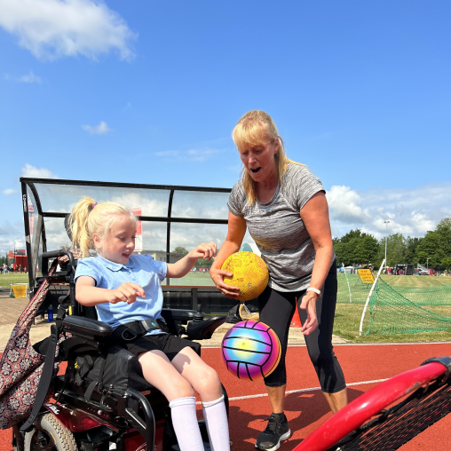 Disabled girl and woman playing with a net and a sports ball on an athletics track. 