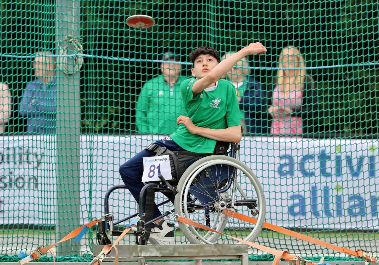 Junior athlete taking part in seated discus throw at Activity Alliance's Athletics Championships event.