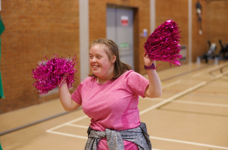 Giel dancing with pom poms in a sports hall. 