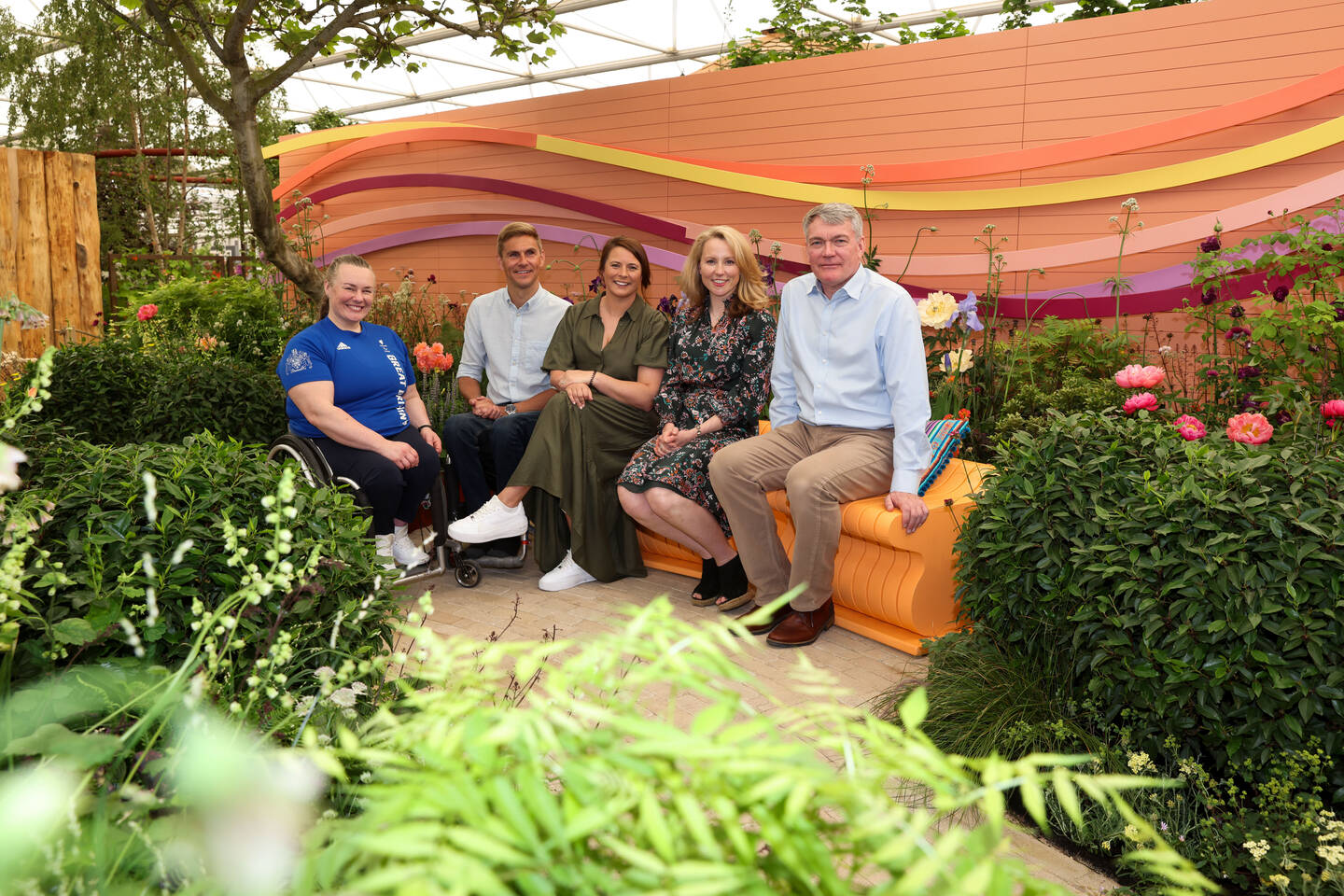 A group of people sit in a garden. They are from left to right Louise Sugden, Steve Brown, Liz Johnson, Penelope Walker and Ashley Iceton.