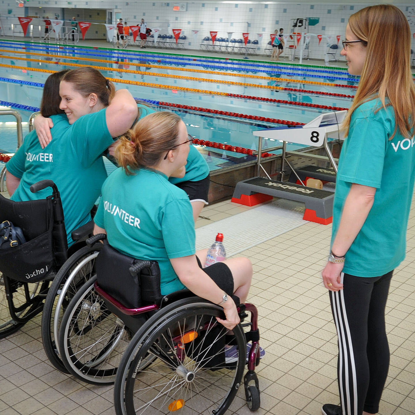 Group of four female volunteers next to a pool. Two are wheelchair users.