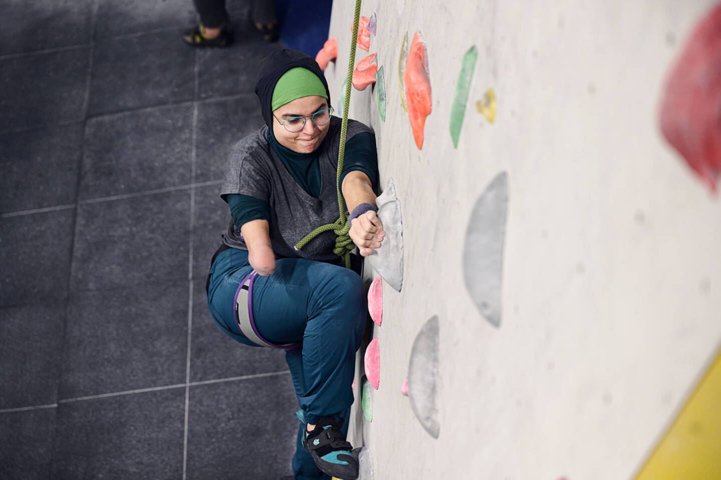 A woman in a headscarf with lower arm limb loss climbs a climbing wall.