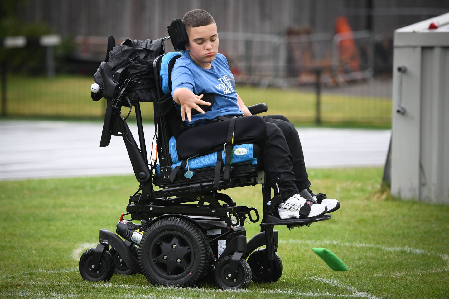 A young boy in a powerchair throws a beanbag as part of an athletics competition