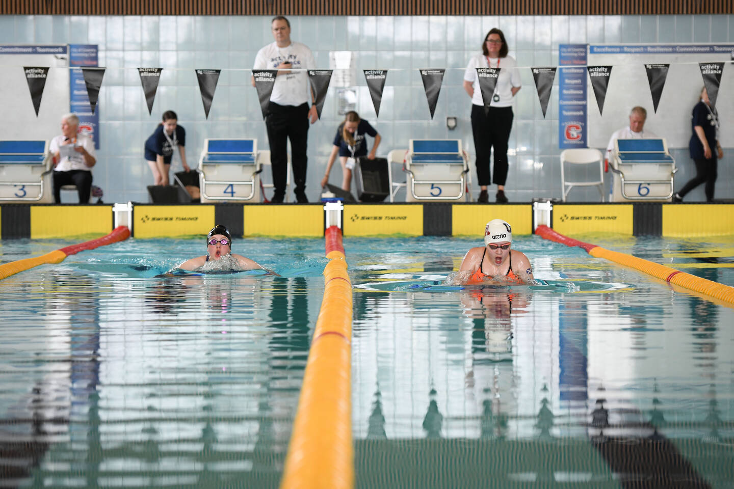 A group of swimmners swim lanes with officials watch on.