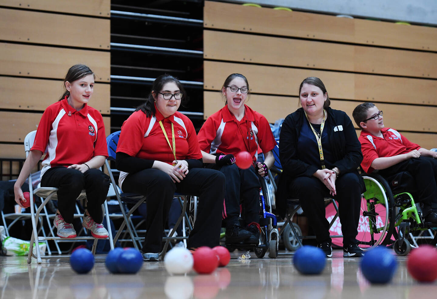 Three girls in red polo shirts play boccia. A woman sits next to them watching.