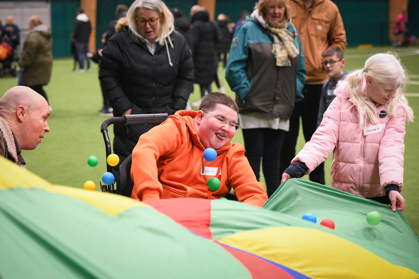 A boy smiles as he plays a parachute game with balls bouncing on top of a multi-coloured sheet.