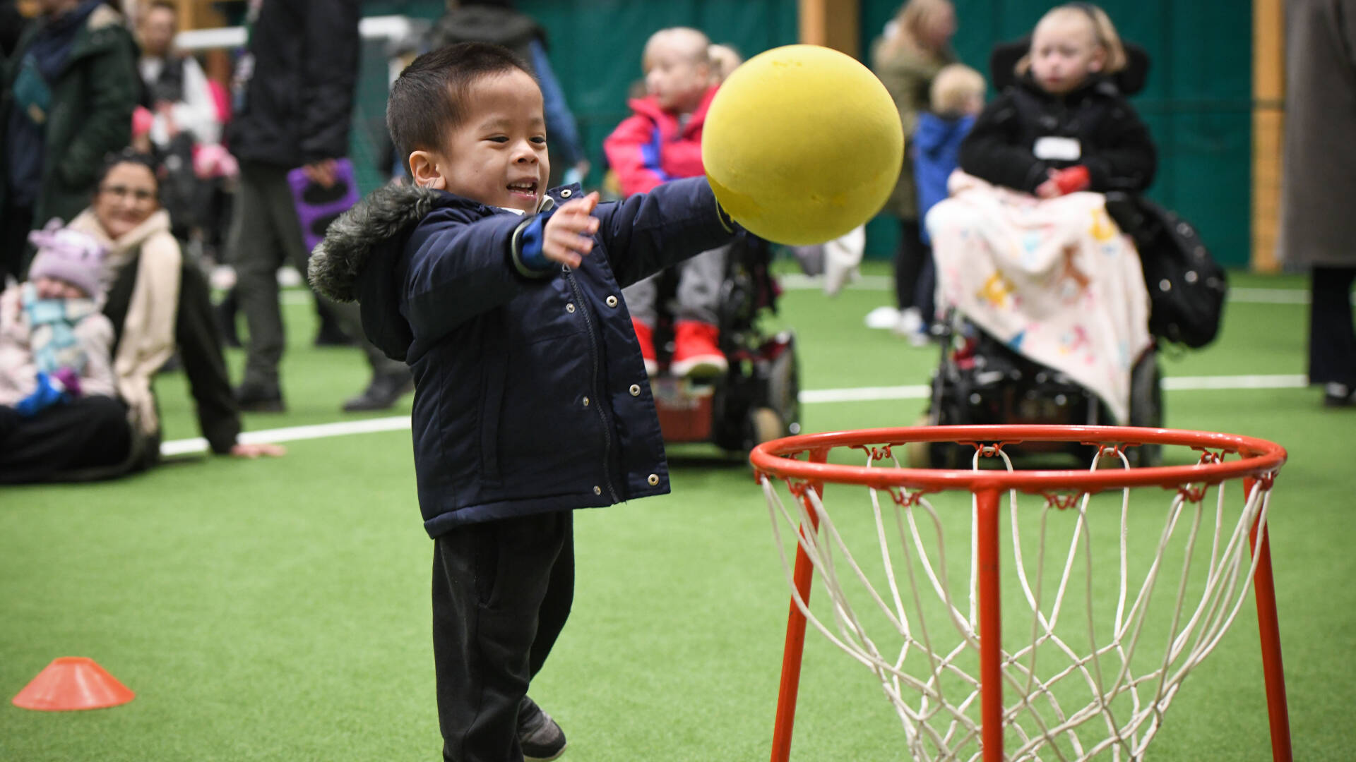 A boy in a coat throws a ball into a net.