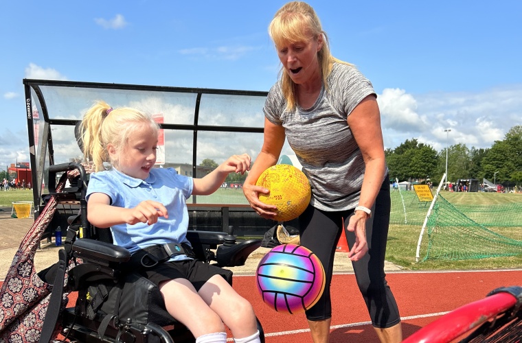 Disabled girl and woman playing with a net and a sports ball on an athletics track.
